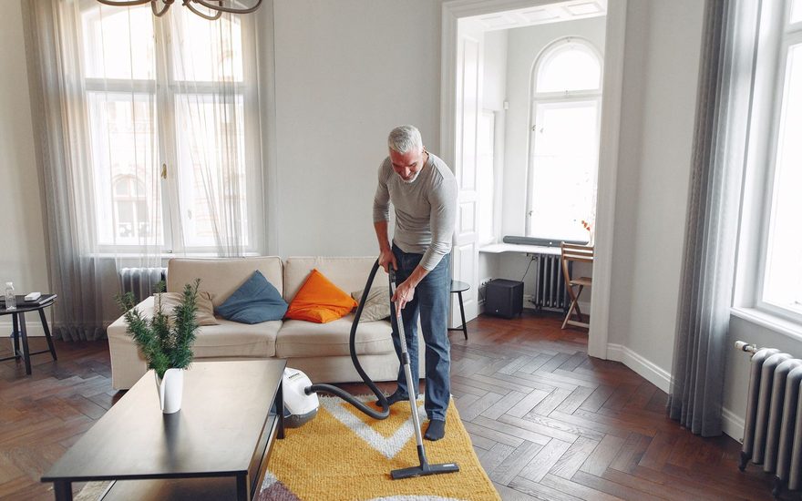 Two men vacuuming a living room carpet